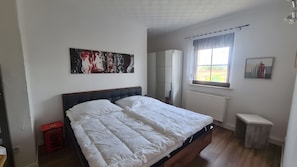 A bedroom with a bed, a radiator, a window with curtains, a wardrobe, and a painting on the wall. - Apartment 'Haus Rose 1' with Shared Garden, Balcony and Wi-Fi (Loddin)