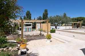 A covered outdoor area with a pergola, potted plants, and a stone pathway.