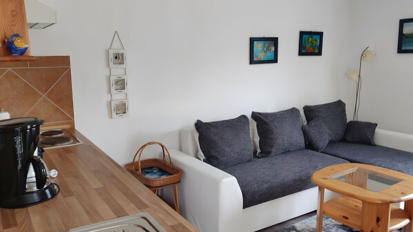A living room with a white sofa, a coffee table, a kettle, a basket, and wall-mounted artwork.