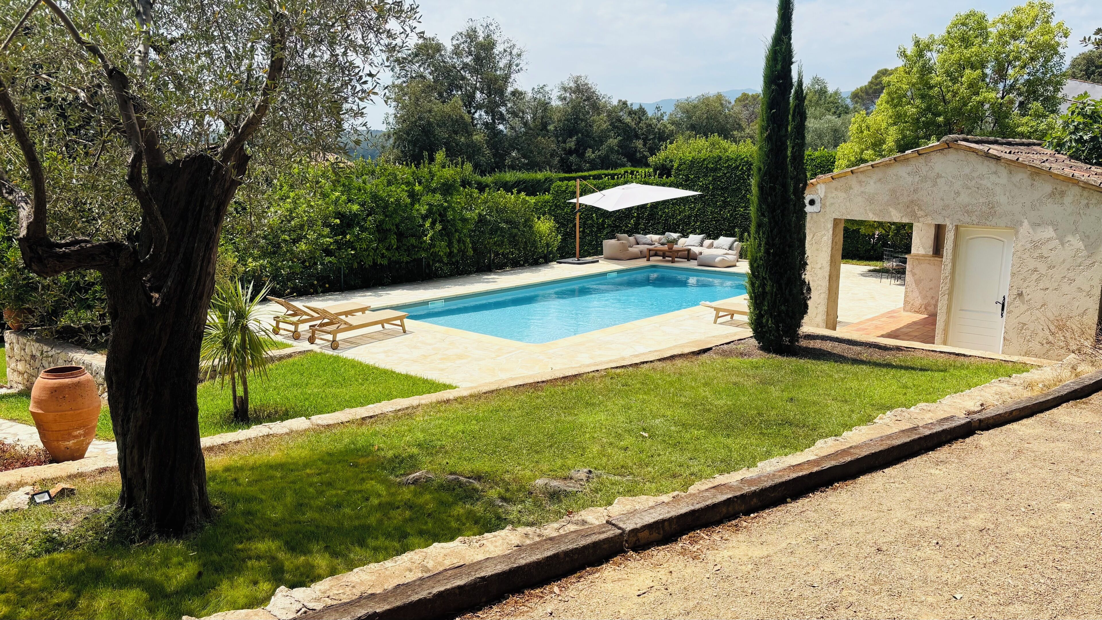 Une piscine avec des chaises longues, un petit jardin et un bâtiment doté d’une porte.