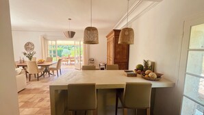 Een keuken met een groot eiland, hangende rieten lampen en een eethoek met stoelen en een tafel.