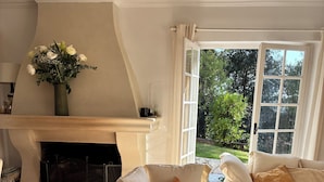 Een woonkamer met een open haard, een bank en uitzicht op groen.