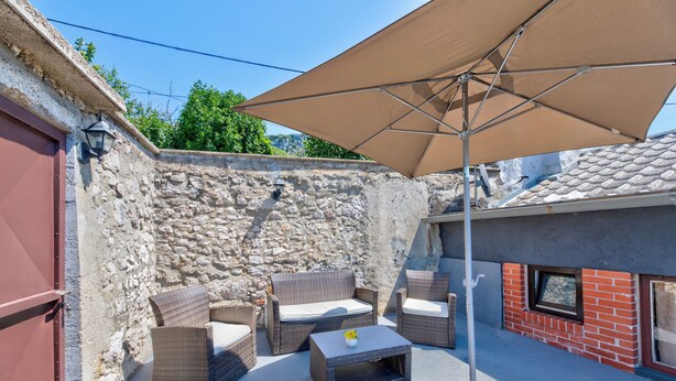 A patio with wicker furniture, a table, and a large umbrella. - Charming vacation apartment with terrace & barbecue in quiet surroundings (Bribir)