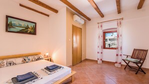 A bedroom with a bed, a wooden headboard, a nightstand, a painting, a window with curtains, and a chair. - Charming vacation apartment with terrace & barbecue in quiet surroundings (Bribir)