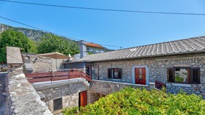 A stone building with a balcony, a red door, and a view of a mountain. - Charming vacation apartment with terrace & barbecue in quiet surroundings (Bribir)