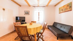 A dining area with a round table, chairs, a sofa, a TV, and a painting on the wall. - Charming vacation apartment with terrace & barbecue in quiet surroundings (Bribir)