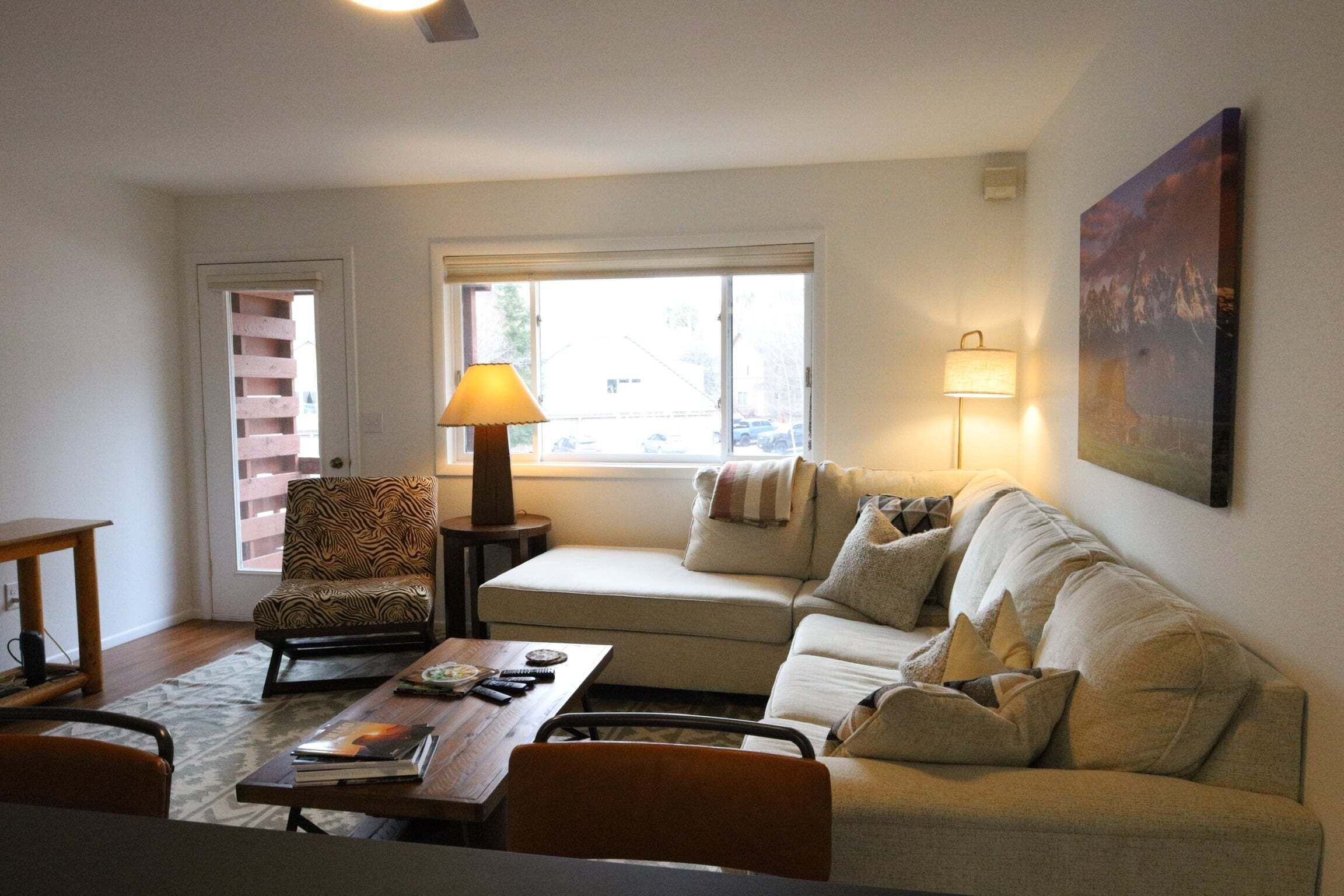 Una sala de estar con un sofá, un sillón, una mesa, una lámpara y un cuadro en la pared.