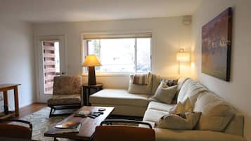 Una sala de estar con un sofá, un sillón, una mesa, una lámpara y un cuadro en la pared.