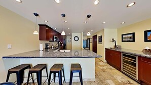 A kitchen with a central island, bar stools, recessed ceiling lights, and a clock on the wall. - 1849 Condos 309 2 Bedroom Condo (Mammoth Lakes)