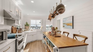 Una cocina moderna con armarios blancos, una mesa de comedor de madera y vista al agua.