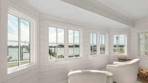 Una habitación con ventanas amplias, una silla blanca y vistas a un cuerpo de agua.