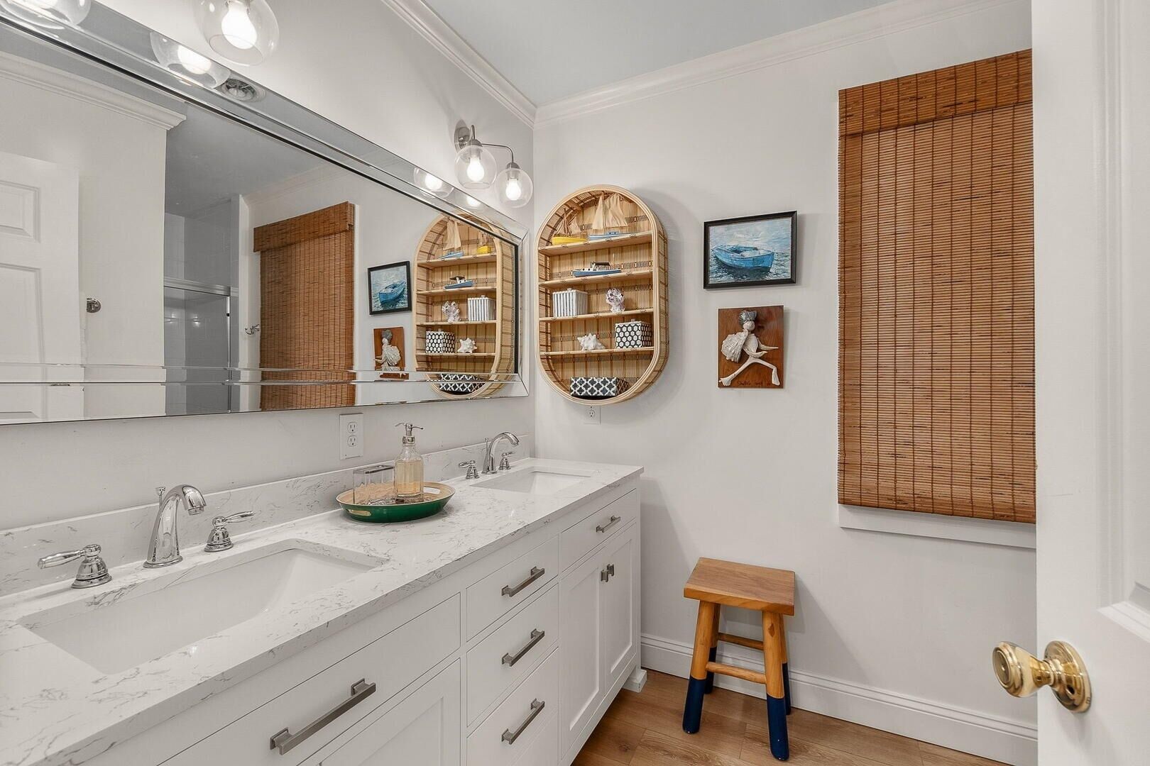 A bathroom with a large mirror, two sinks, wooden shelves, and a small stool.