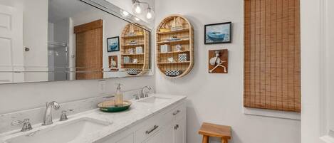 A bathroom with a large mirror, two sinks, wooden shelves, and a small stool.