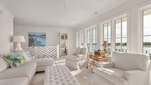 Un salón amplio con una decoración en blanco, ventanas grandes y vistas al agua.