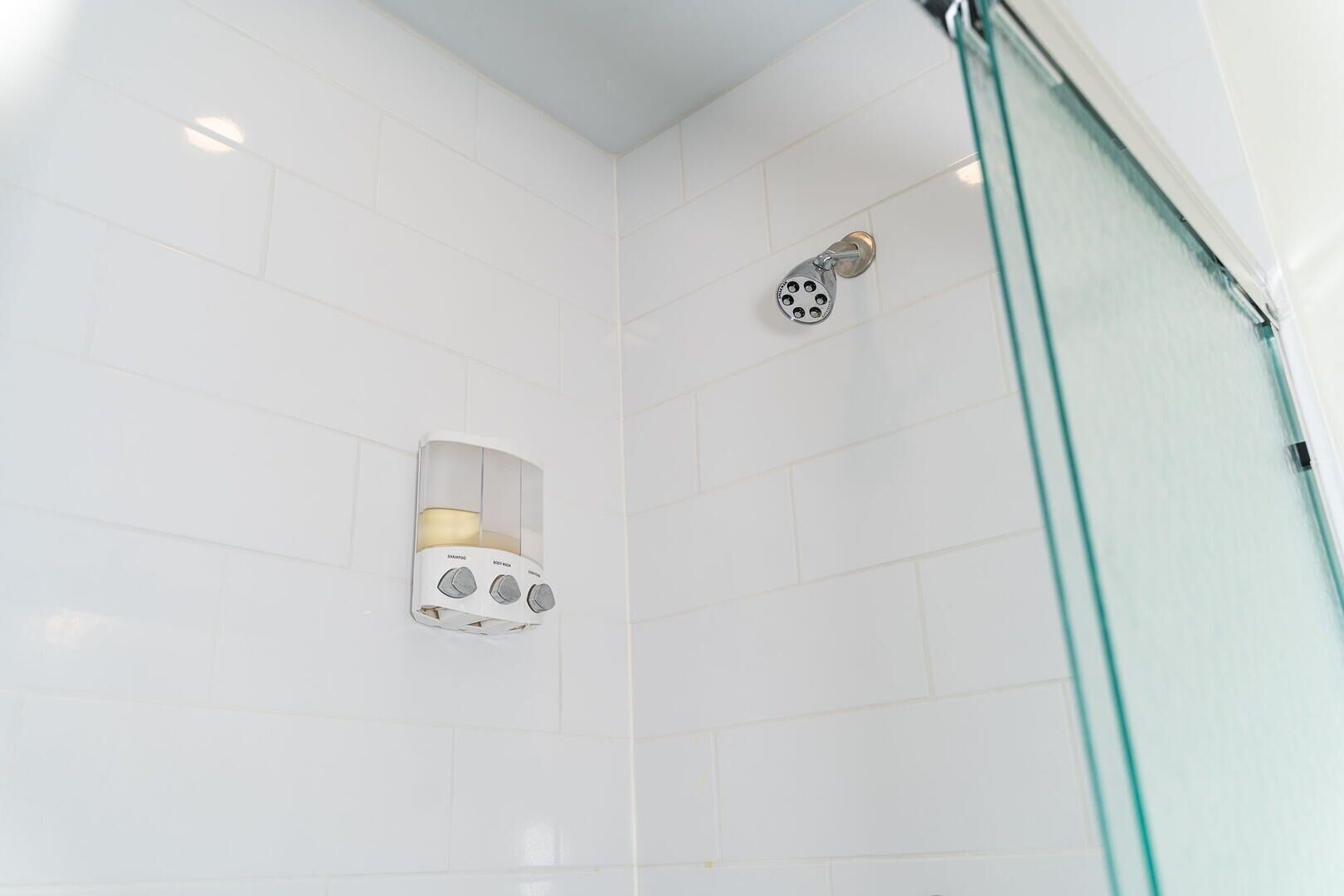 A shower with a handheld showerhead, a wall-mounted soap dispenser, and a glass shower enclosure.
