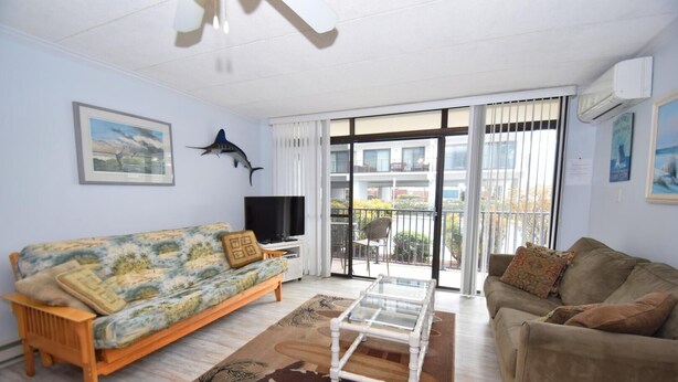 A living room with a sofa, a glass coffee table, a TV, and a balcony with a view. - Eldorado 2 1 Bedroom Condo (Ocean City)
