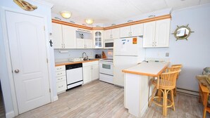 A kitchen with white cabinets, a dishwasher, a stove, and a small island with chairs. - Eldorado 2 1 Bedroom Condo (Ocean City)