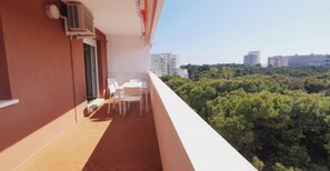 Un balcon avec une table et des chaises, un appareil de climatisation et une vue sur le paysage urbain et les arbres.