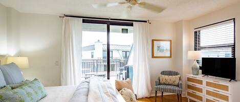 A bedroom with a bed, a TV, a dresser, a chair, and a balcony.