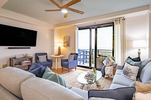 Een woonkamer met een bank, fauteuils, een salontafel, een televisie, een plafondventilator en een balkon met uitzicht.