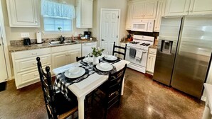 Une cuisine avec des meubles blancs, un réfrigérateur en acier inoxydable, une cuisinière à gaz et une table à manger pour quatre personnes.