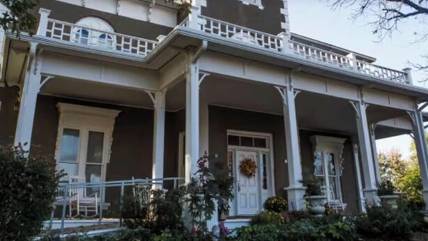 Une maison à deux étages avec un porche, des colonnes et une porte d’entrée.