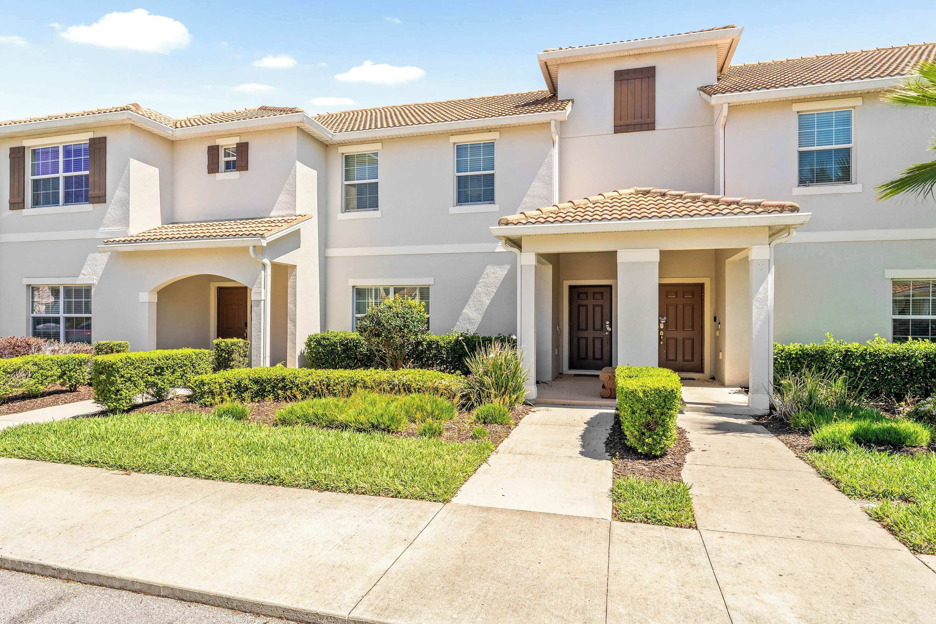 A multi-story residential building with a tiled roof, a front porch, and a landscaped garden.
