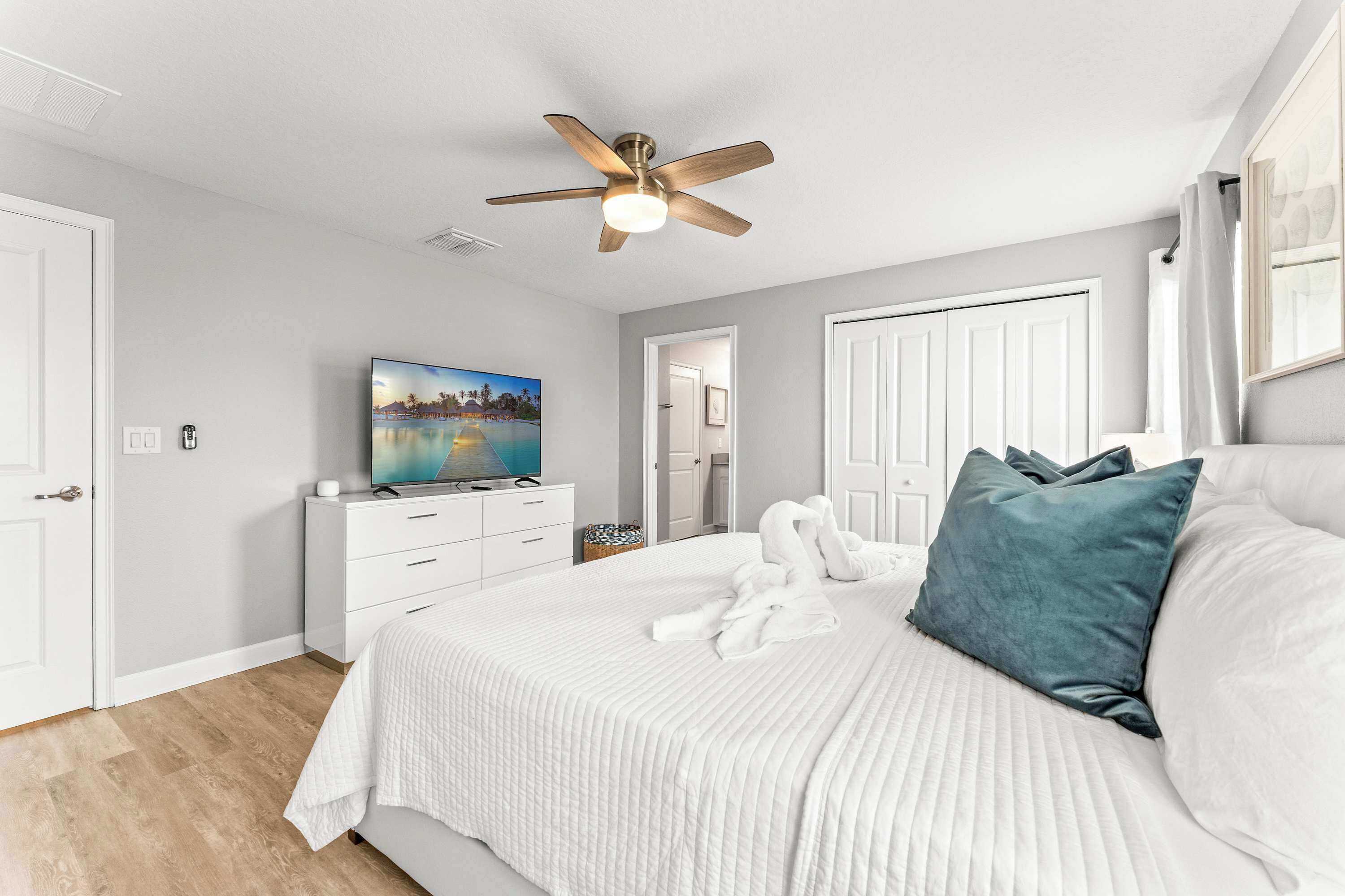 A bedroom with a bed, a ceiling fan, a TV, and a door.