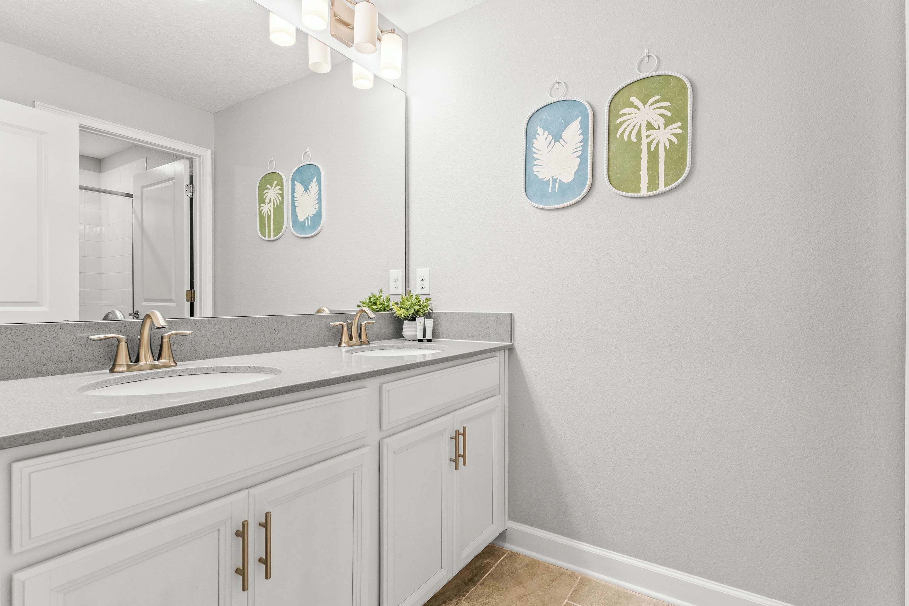A bathroom with a double sink vanity, a mirror, and wall-mounted artwork.