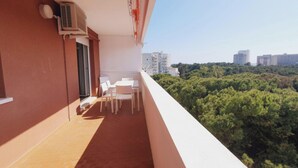 Un balcone con tavolo e sedie, un condizionatore d'aria e vista sulla città e sugli alberi.