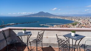 Eine Terrasse mit Metallstühlen und -tischen mit Blick auf eine Küstenstadt und einen markanten Berg in der Ferne.