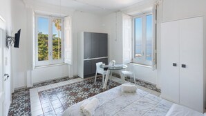 A room with a bed, a small table with chairs, a wardrobe, and a window with a view. - Apartment 'La Finestra' with Sea View, Wi-Fi and Air Conditioning (Castellammare di Stabia)