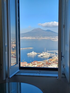 A view through an open window of a marina with yachts, a mountain in the background, and a coastal cityscape. - Apartment 'La Finestra' with Sea View, Wi-Fi and Air Conditioning (Castellammare di Stabia)