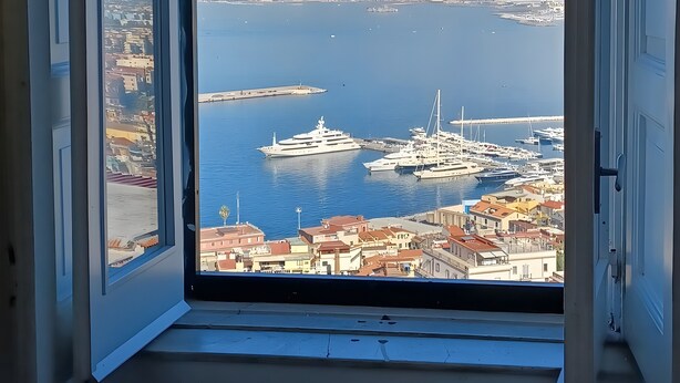 A view through an open window of a marina with yachts, a mountain in the background, and a coastal cityscape. - Apartment 'La Libreria' with Mountain View, Wi-Fi and Air Conditioning (Castellammare di Stabia)