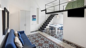 Un soggiorno moderno con un divano, una scala che conduce a una sala da pranzo e un televisore a schermo piatto montato a parete.