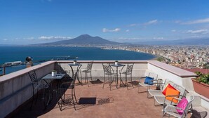 Una terrazza con posti a sedere all'aperto, vista su una città costiera e una montagna in lontananza.