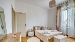 Ein Schlafzimmer mit einem Bett, Nachttischen, einem runden Teppich und einem Fenster mit Vorhängen.