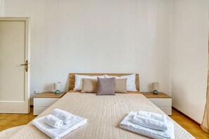 Une chambre d’hôtel avec un lit, deux tables de chevet, une commode et une porte.