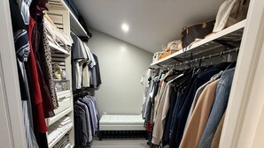Ein schmaler Durchgangsschrank mit Regalen, hängender Kleidung, einer Bank und einem Schuhregal.