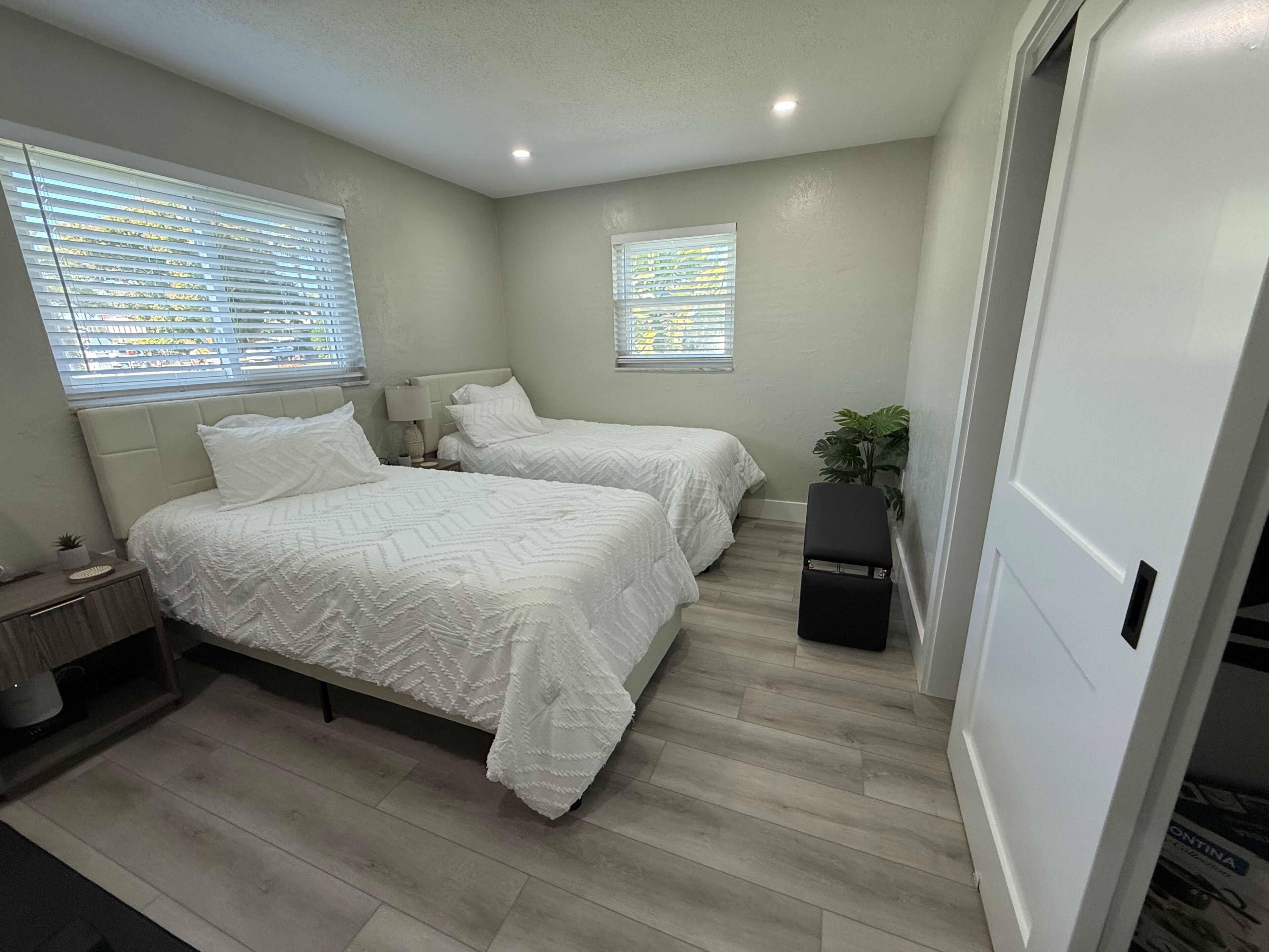 A bedroom with two beds, a nightstand, a lamp, and a potted plant.