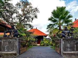 A pathway leading to a building with a red roof, flanked by statues and surrounded by greenery. - Wahyu Dewata Villa (Gianyar)