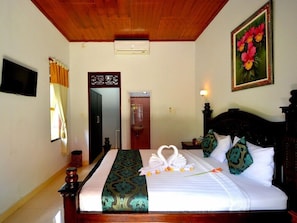 A hotel room with a bed, a painting, a door, and a ceiling fan. - Wahyu Dewata Villa (Gianyar)