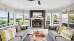 Ein Wohnzimmer mit Kamin, zwei Sofas, einem Couchtisch und großen Fenstern mit Blick ins Freie.