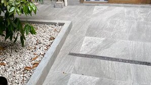 A modern building entrance with a stone pathway, a wooden door, and a large green plant. - Studio | 5 min from airport | 100 m from beach | Beto Carrero World (Navegantes)
