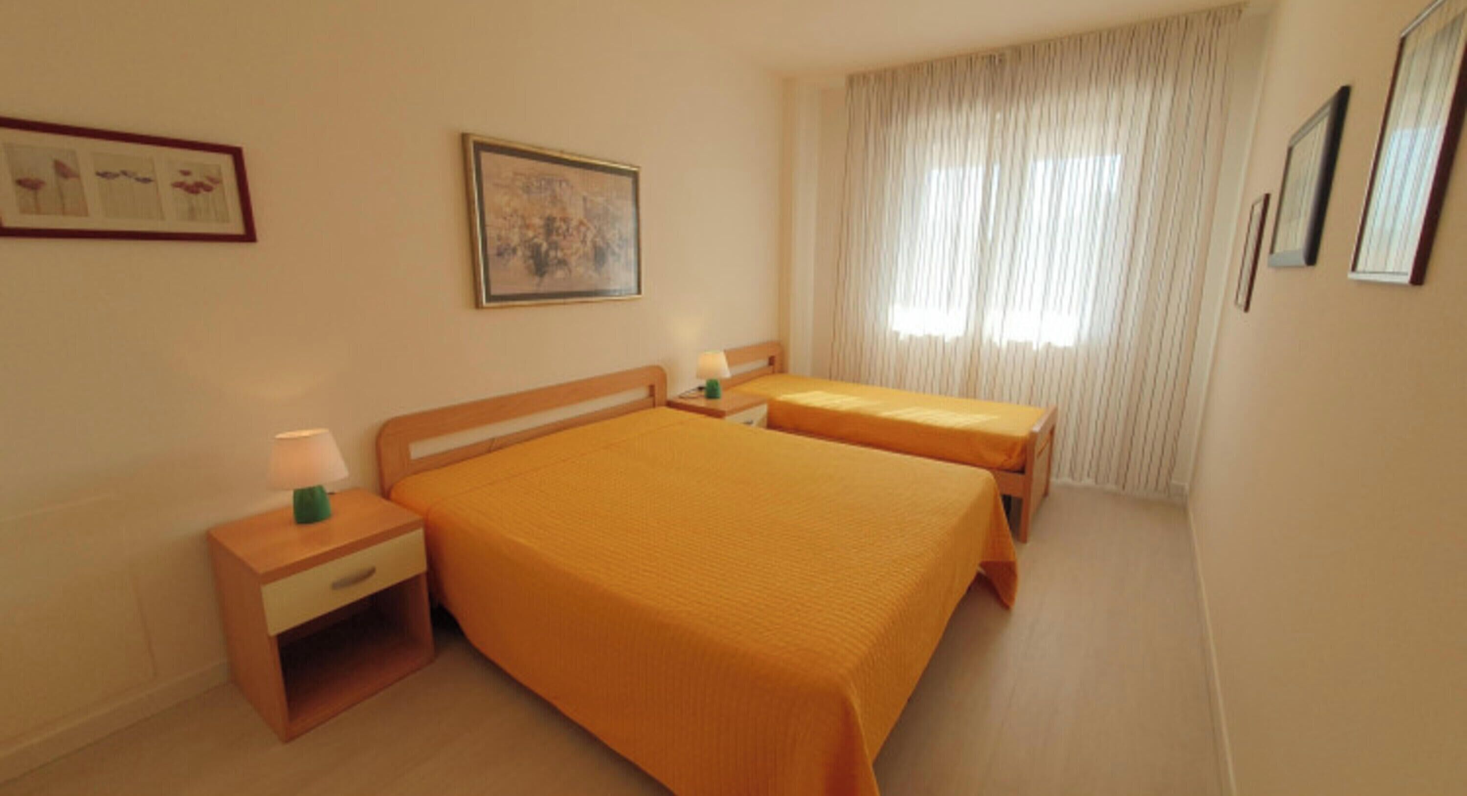 A hotel room with two beds, a nightstand, a lamp, a framed picture, and a window with curtains.