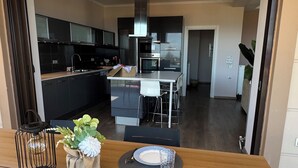 Ruokailutilassa on puinen pöytä, joka on katettu kahdelle, taustalla näkyy keittiö ja ovi johtaa toiseen huoneeseen.