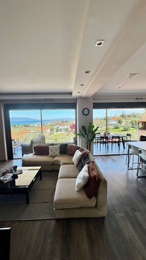 Ein geräumiges Wohnzimmer mit einer großen Eckcouch, einem Essbereich und Blick auf eine Küstenlandschaft.