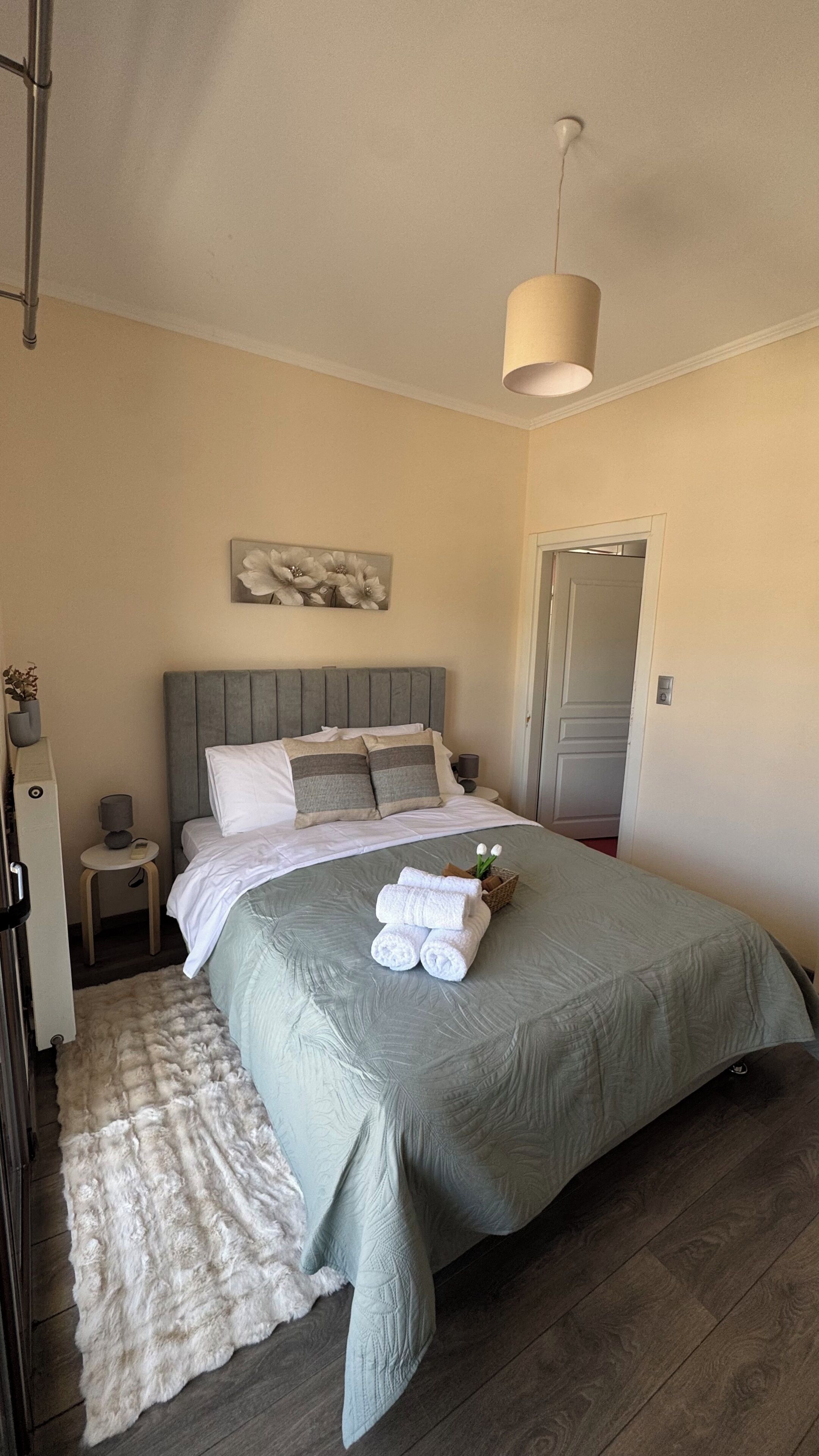A bedroom with a bed, a bedside table, a lamp, a painting on the wall, and a door.