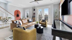 Una sala de estar moderna con un sofá, sillones, una mesa de centro, un ventilador de techo y un televisor.