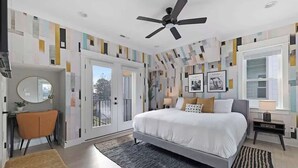 Un dormitorio moderno con cama, ventilador de techo, escritorio, silla y un amplio ventanal.